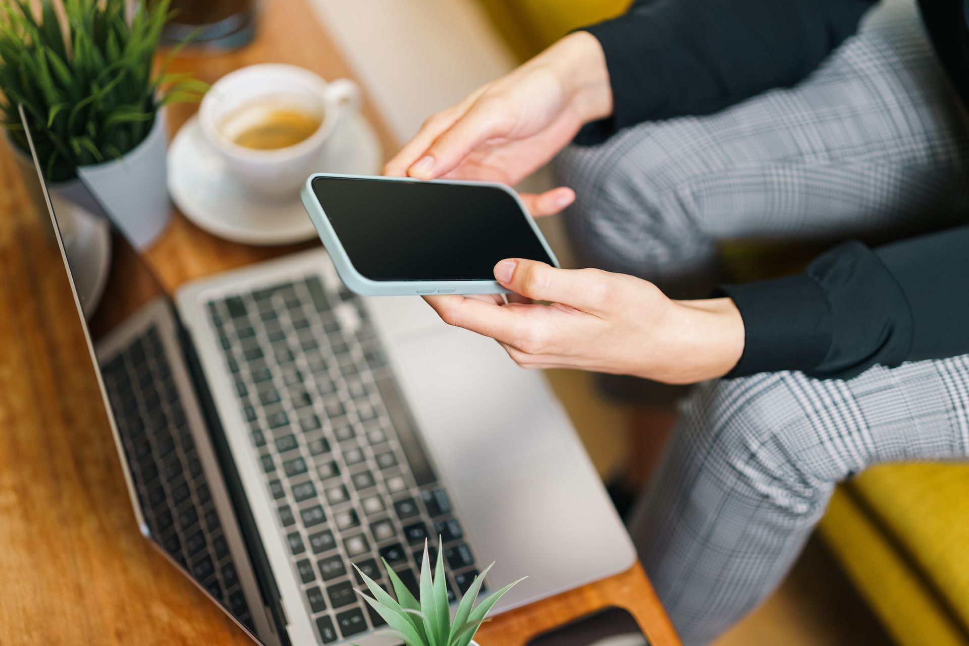 Hands using a smartphone above a laptop at a desk